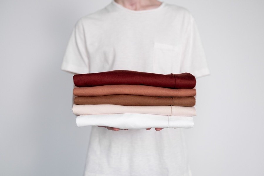 Neutral folded shirts being held before wardrobe organization.