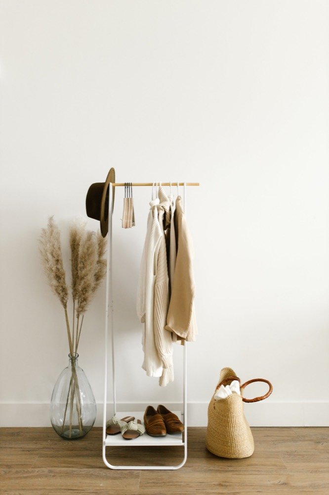 Neutral knitwear, shoes, and wardrobe pieces arranged on a clothing rail.